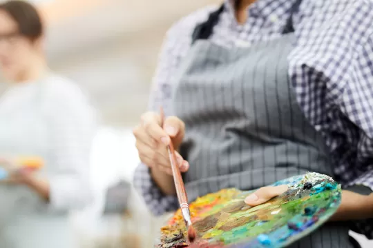 A close up of a woman painting and her paint palette.