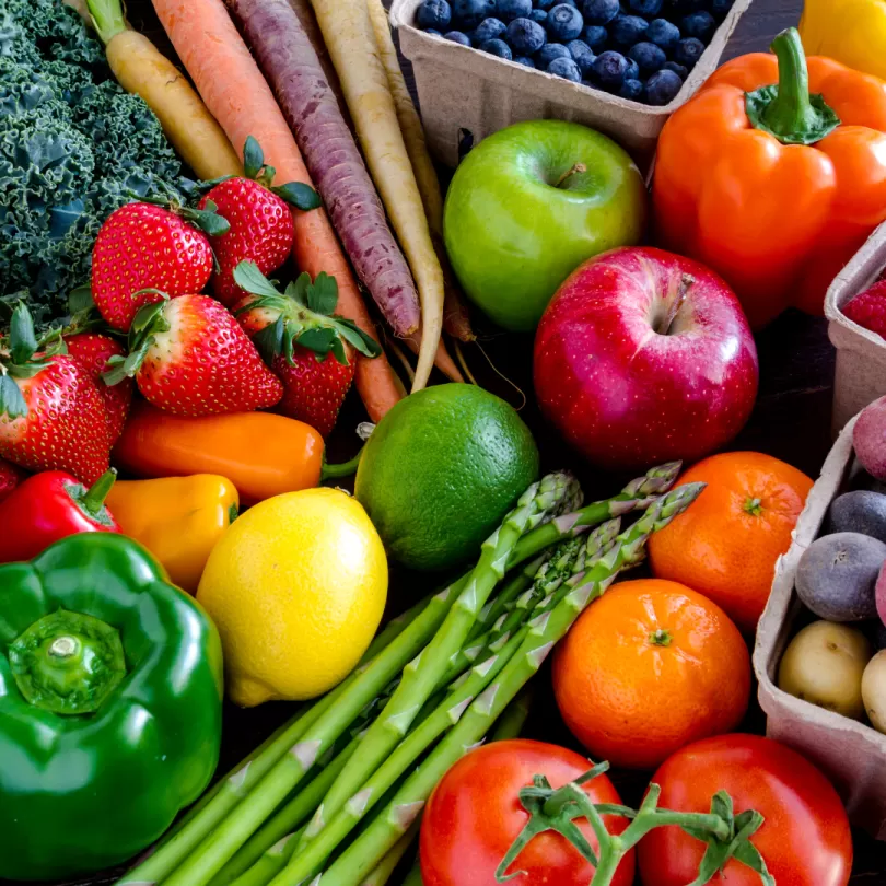 A flat lay of a large variety of fruits and vegetables. There are bell peppers, lemons, limes, apples, asparagus, tomatoes, berries, and carrots.