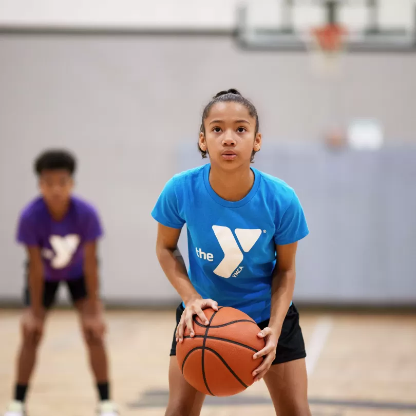 A girl wearing a blue shirt concentrates as she prepares to shoot a basketball.