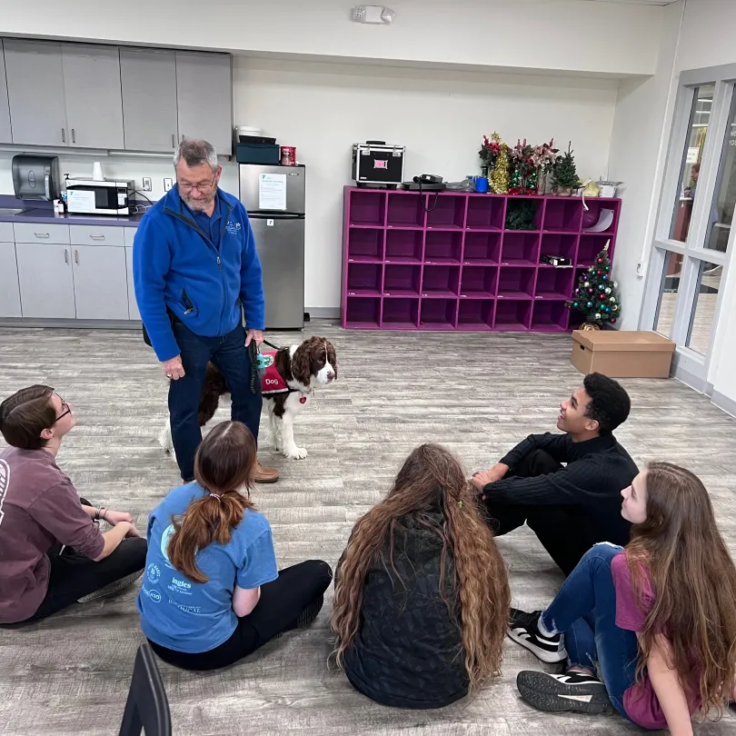 Teens sitting around presenter with service dog