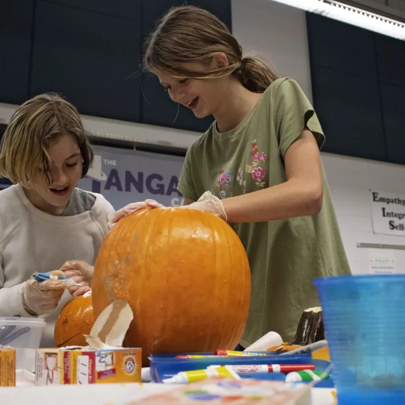 Middle school aged kids carve pumpkin in school like setting