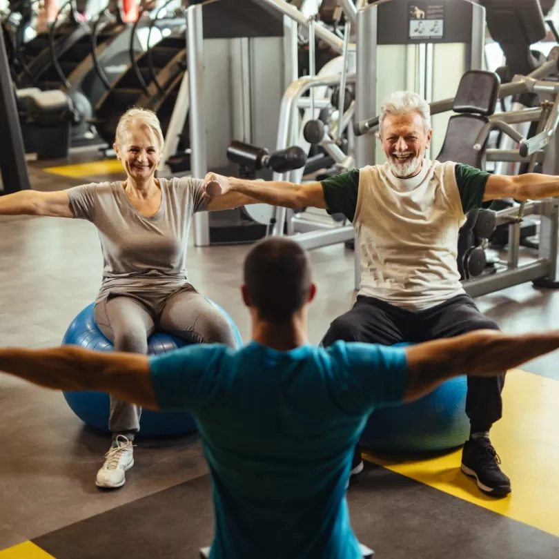 Man and woman lifting weights at the direction of a personal trainer