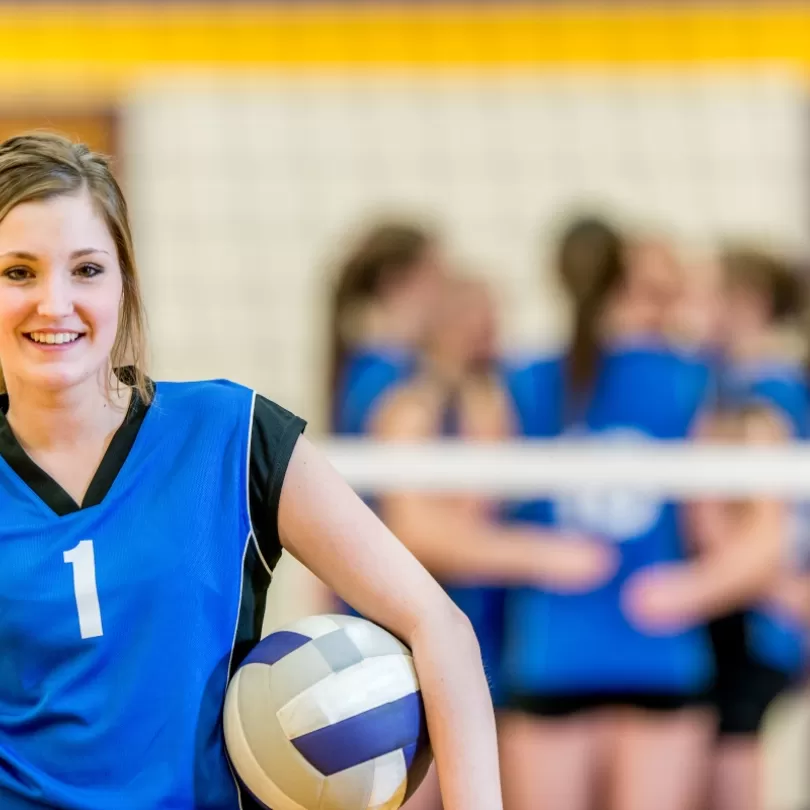 Girl with Volleyball under arm with team in background