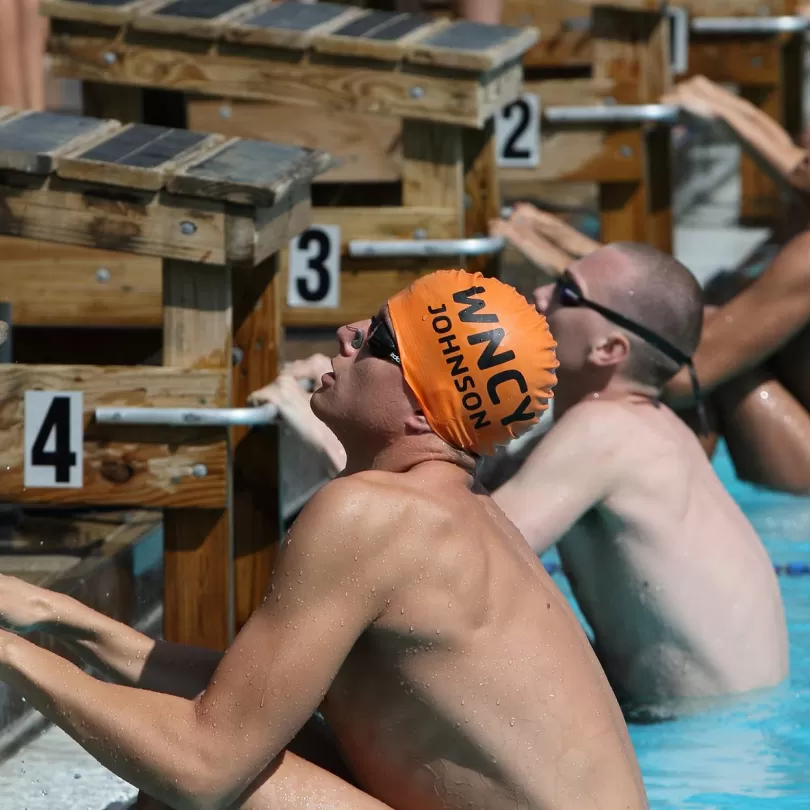 Several swimmers line up on the starting block ready for backstroke 