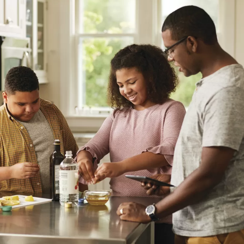 Three people of color stand around a kitchen island cooking a healthy meal together