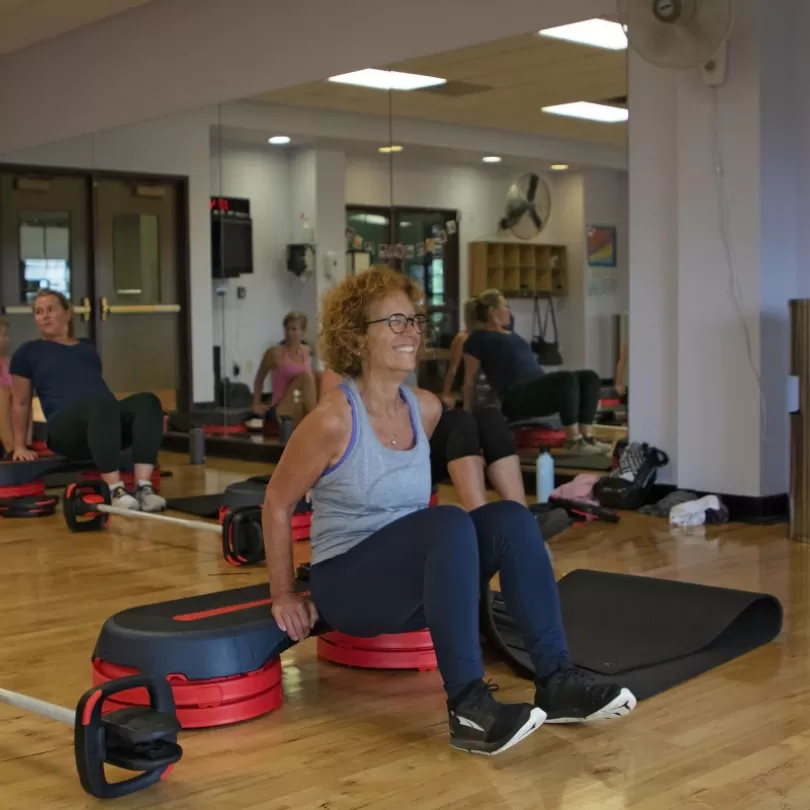 Woman doing triceps exercise using a less mills step and dipping, others are in the background doing the same exercise during a group class. 