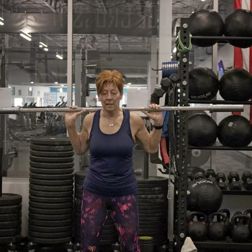 Healthy aging woman lifting barbell with several weights in the background