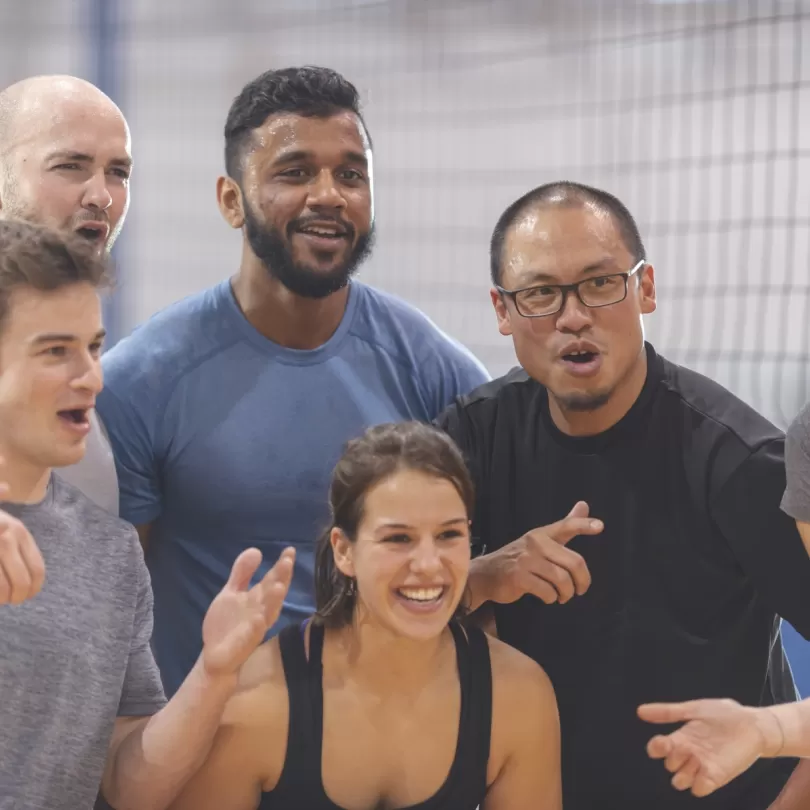 Diverse group of people laughing and posing for a photo in front of what appears to be a volleyball net