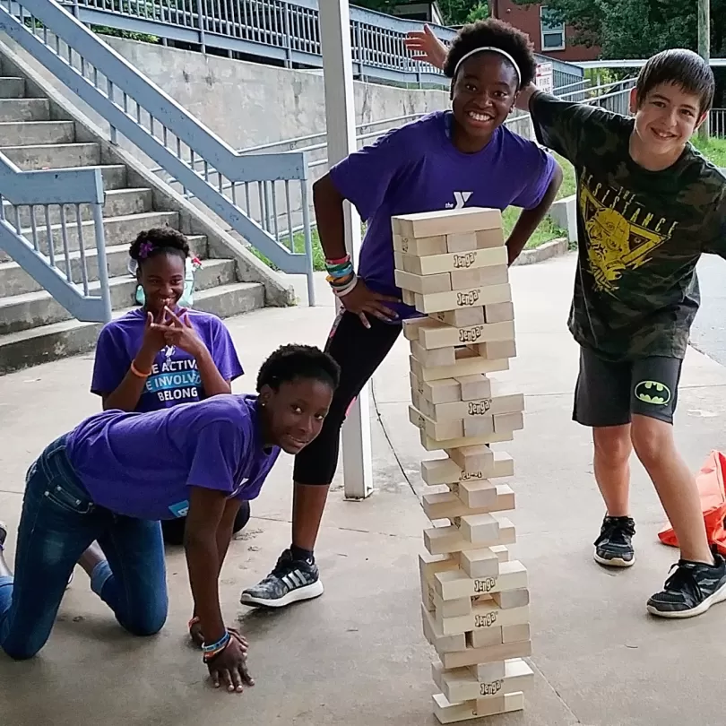 Four pre-teen kids play oversized jenga. All are laughing and looking at the camera.