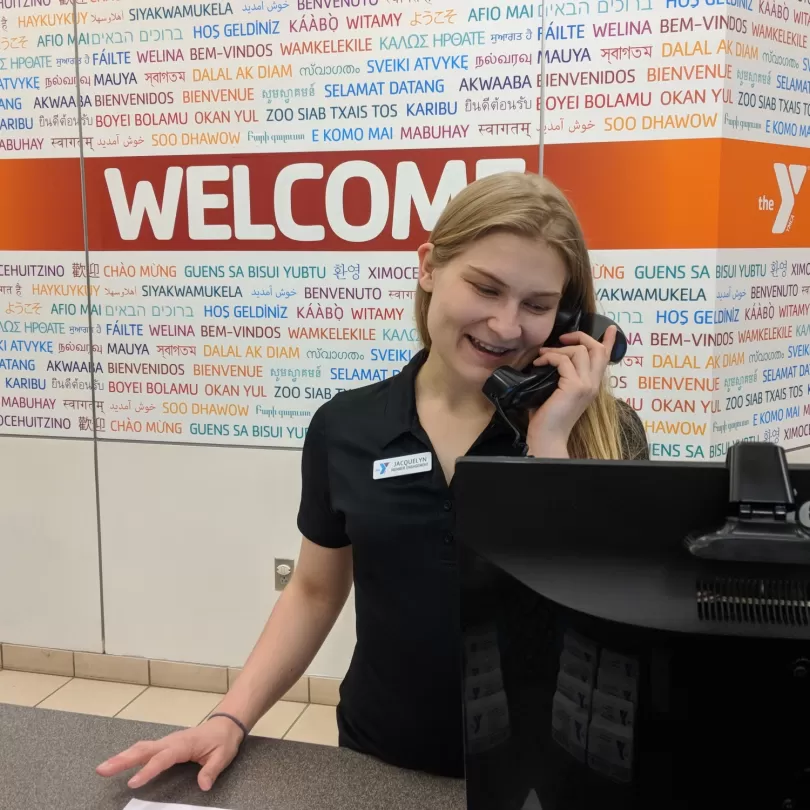 Woman on the phone at a front desk with a Y Welcome sign in the background