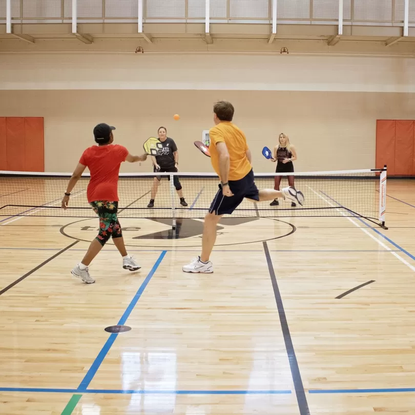 two pickleball teams play a competitive match, one person is jumping in the air to go after the ball