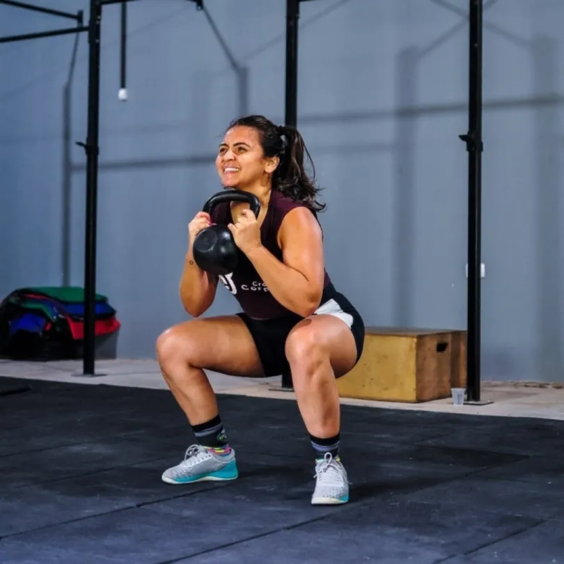 A woman smiles as she lifts a kettlebell in her CrossFit class.