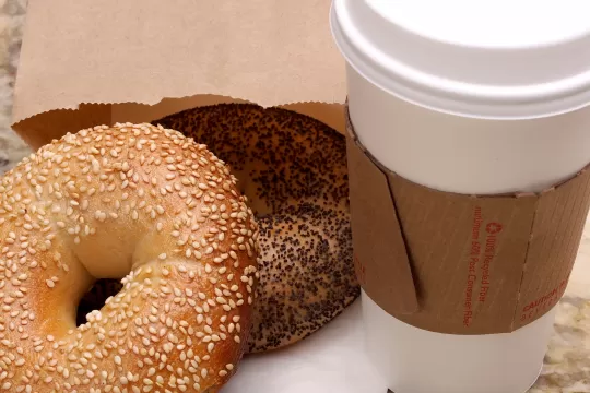 Two bagels lie on top of a napkin. A paper cup of coffee sits next to them on a countertop.