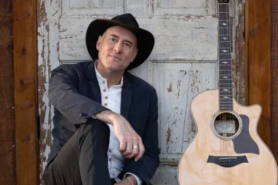 A picture of David LaMotte. He is sitting on the ground next to his guitar.