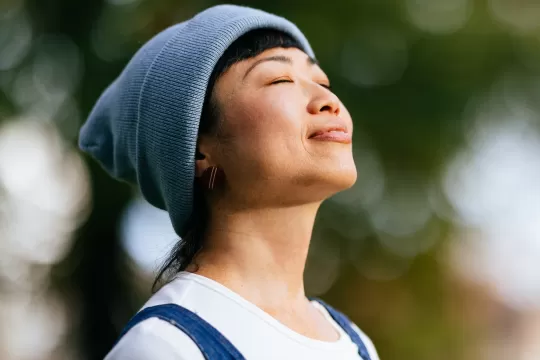 A woman stands outside with her eyes closed. She has a content expression on her face.