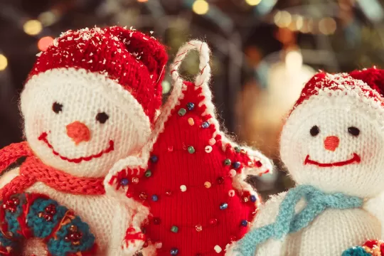 A close up picture of handmade holiday crafts. There are two stuffed snowmen and a red stuffed Christmas tree.