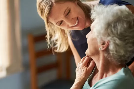 Elderly woman with caregiver. They are smiling at each other.