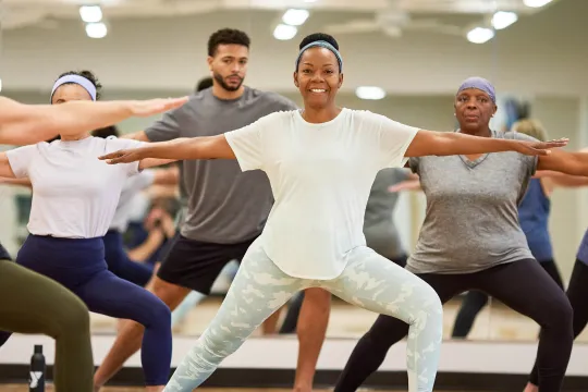 A woman smiles at the camera as she poses during an indoor group exercise class.