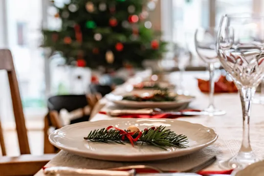 A close up of a holiday dinner place setting with decorations in the background.