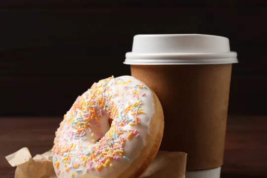 A doughnut next to a cup of coffee on a table.