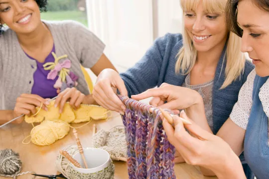 A group of women smile as they do crafts together at a table.