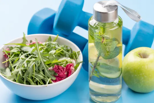 A picture of salad, water, an apple, and weights representing a healthy lifestyle.
