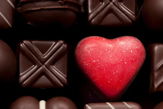 A box of different types of chocolates focusing on a heart-shaped chocolate.