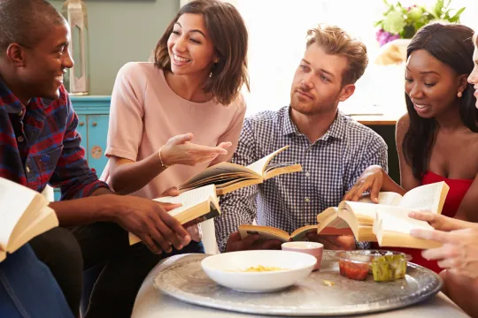 A group of people smile as they discuss a book during a book club meeting.