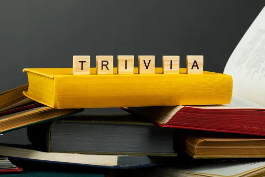 Wooden blocks that spell "Trivia" sit on top of a pile of books.