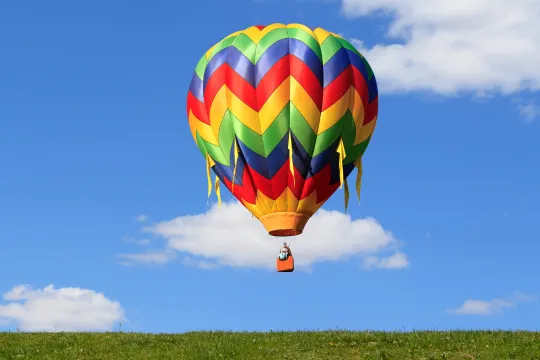 A hot air balloon floats above the ground on a sunny day.