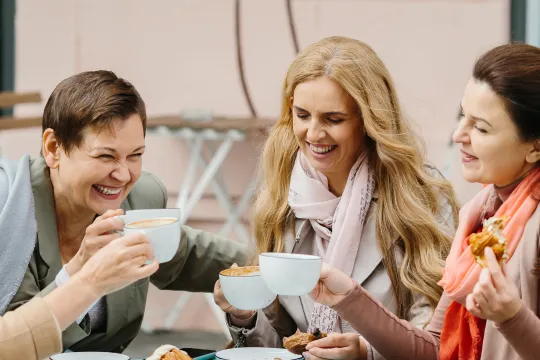 A group of women laugh as they eat outside.