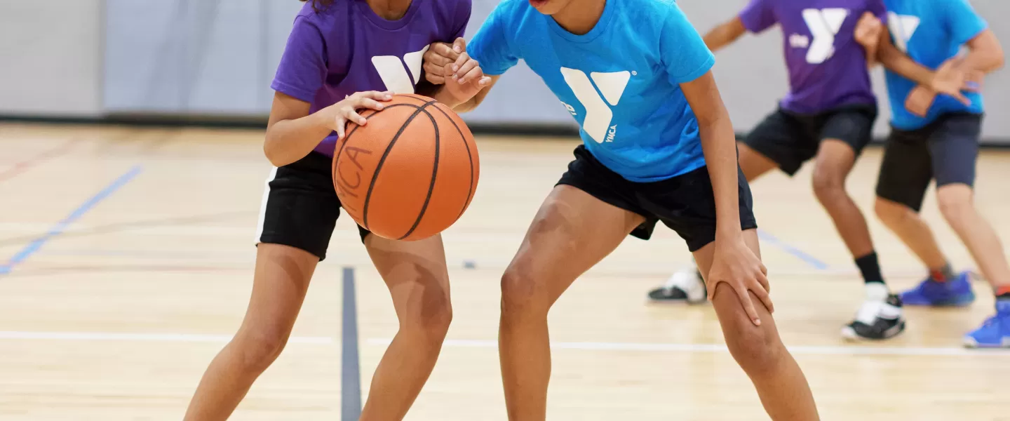 Two girls play basketball in a gym.