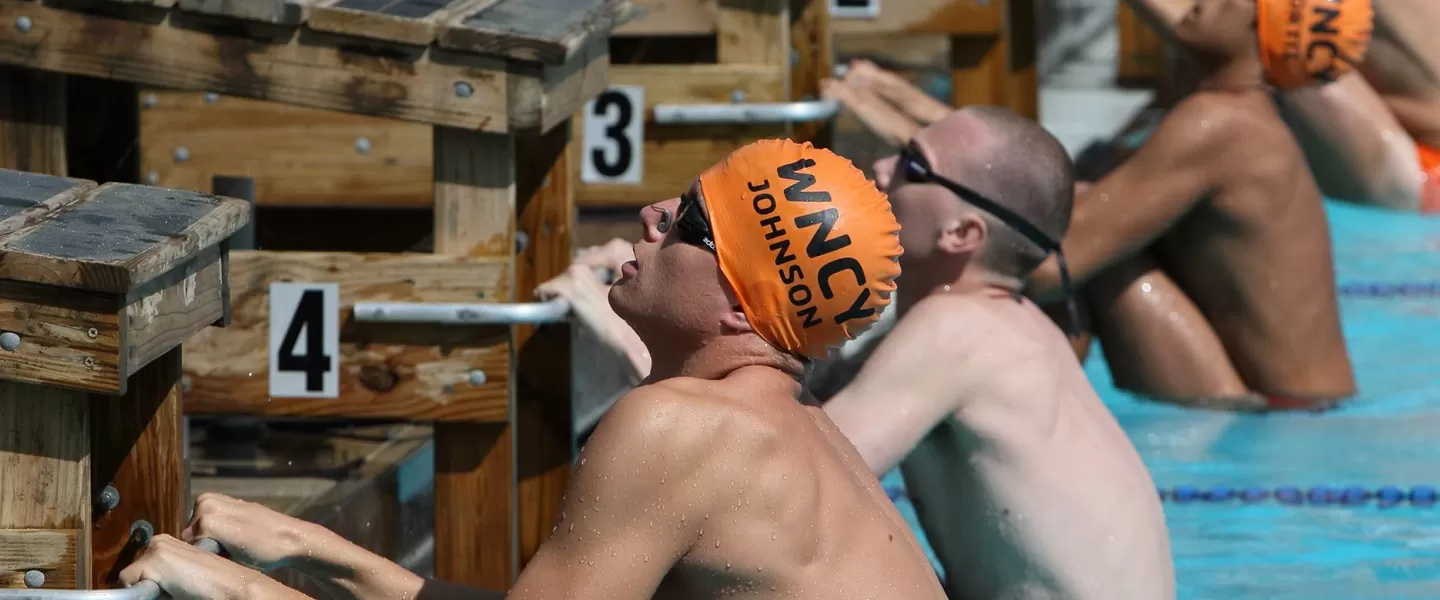 Several swimmers line up on the starting block ready for backstroke 