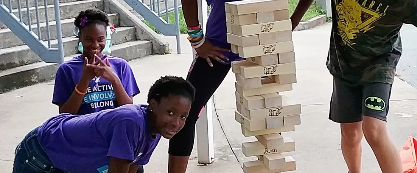 Four pre-teen kids play oversized jenga. All are laughing and looking at the camera.