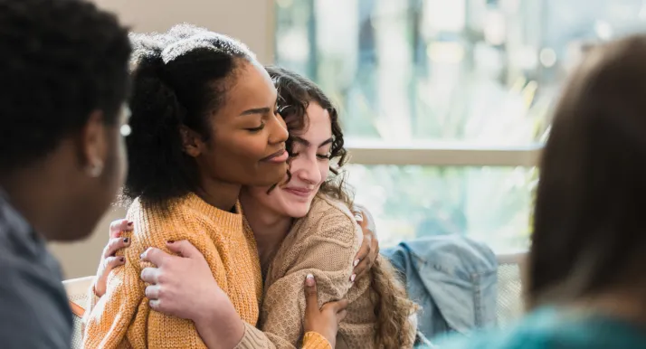Two teenage girls hug each other as they sit in a teen support group session.
