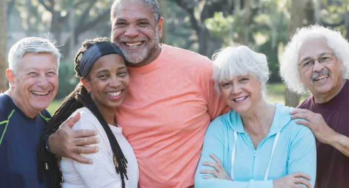 A group of older adults smile and embrace each other outside.