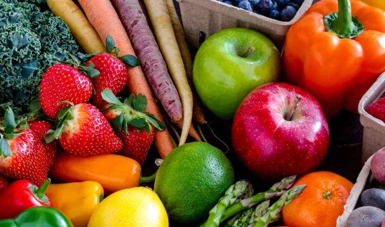 A flat lay of a large variety of fruits and vegetables. There are bell peppers, lemons, limes, apples, asparagus, tomatoes, berries, and carrots.