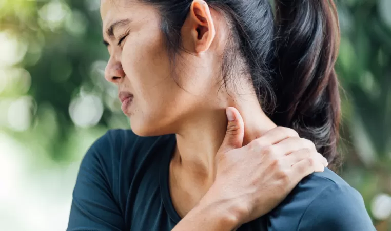 A woman with neck pain rubs her shoulder.