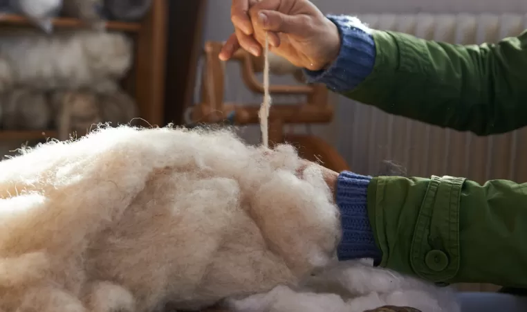 A pair of hands pull wool from a basket to make yarn.