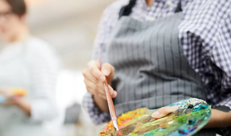 A close up of a woman painting and her paint palette.