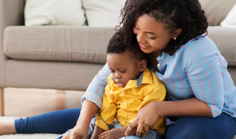 A teenage girl sits on the floor and plays with a baby while she babysits.