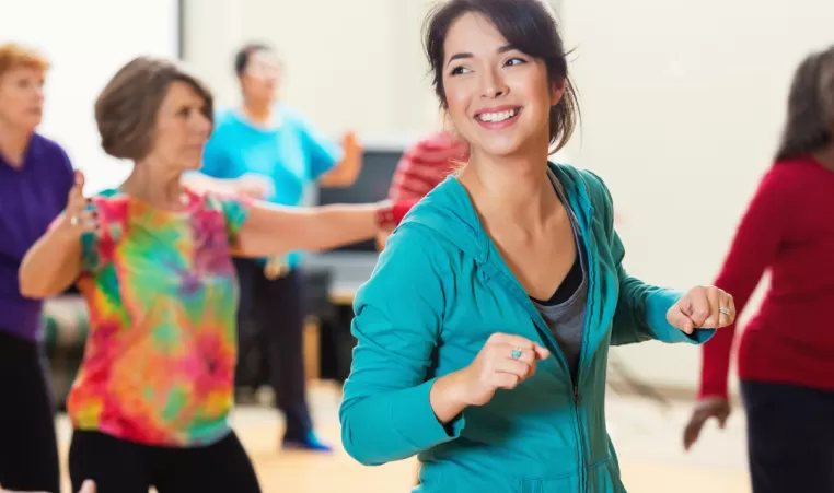 A woman smiles as she line dances with others in a dance class.