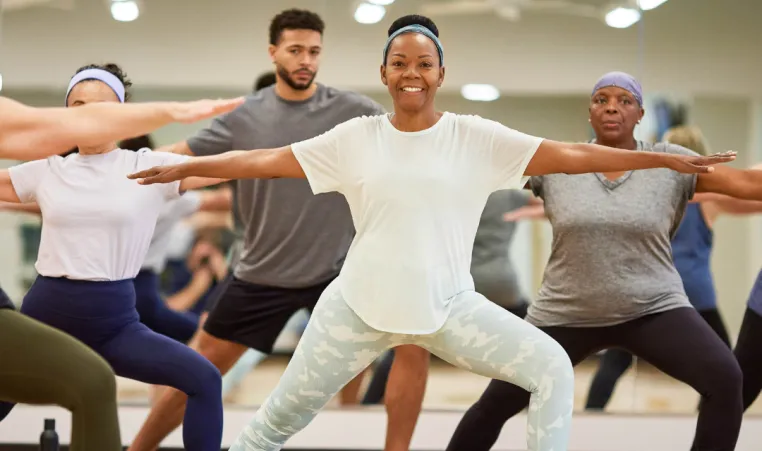 A woman smiles at the camera as she poses during an indoor group exercise class.