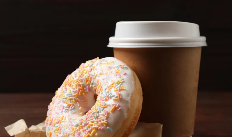 A doughnut next to a cup of coffee on a table.