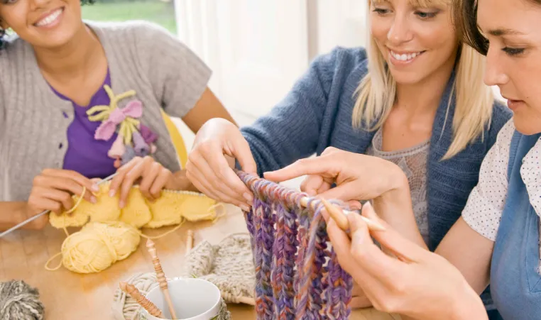 A group of women smile as they do crafts together at a table.