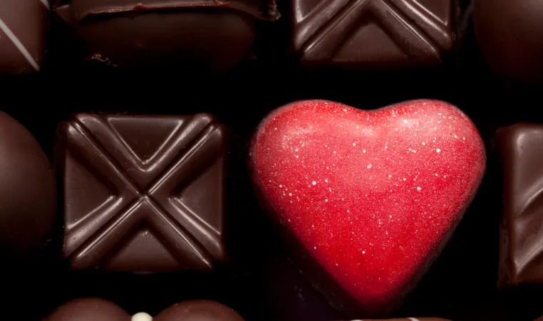 A box of different types of chocolates focusing on a heart-shaped chocolate.