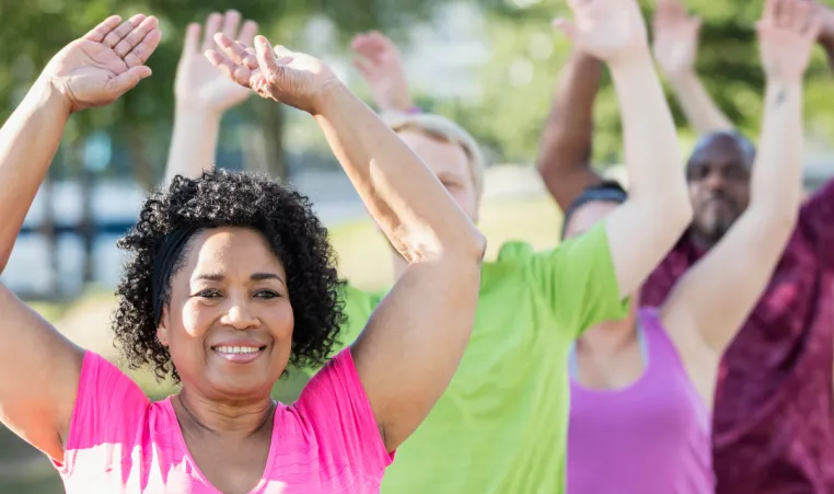 A woman smiles as she exercises in a group outside.