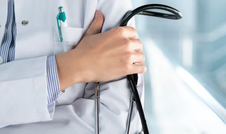 A close up abstract picture of a doctor. Their arms are crossed and they are holding a stethoscope in one hand.