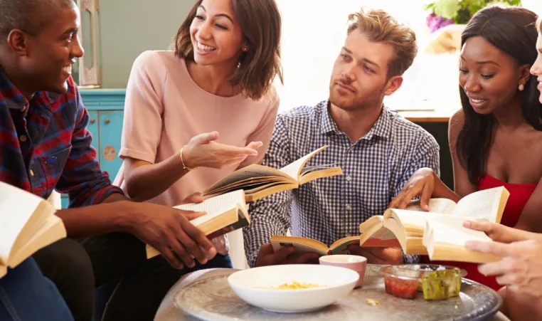 A group of people smile as they discuss a book during a book club meeting.