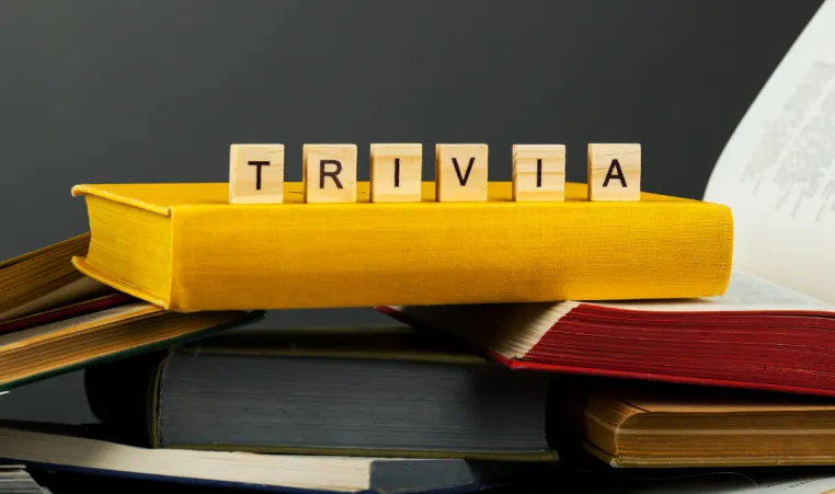 Wooden blocks that spell "Trivia" sit on top of a pile of books.